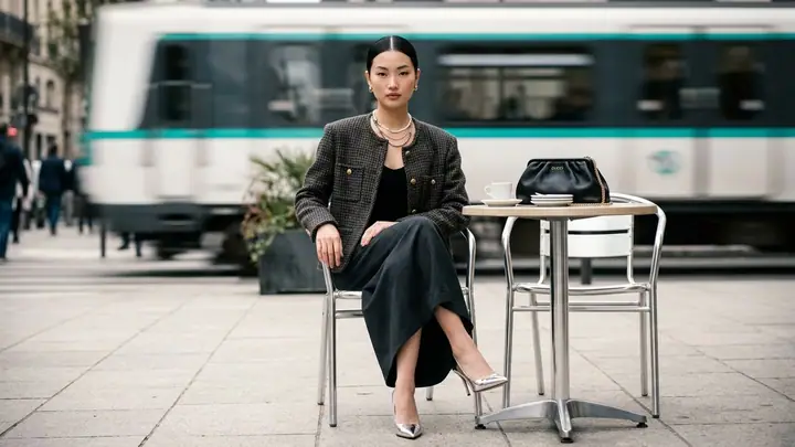 Woman in a tweed jacket seated on a chrome chair at a sidewalk café