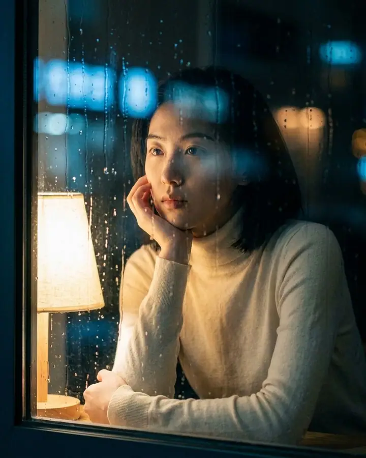 AI example of a woman behind a rain-streaked window with blurred city lights