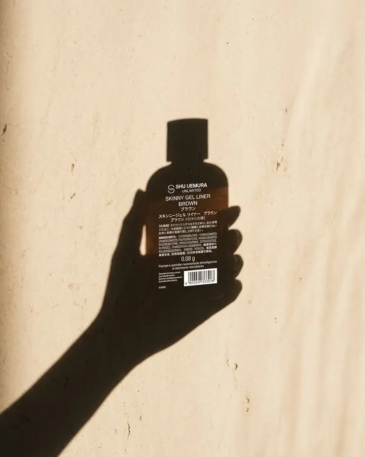Shadow of a hand holding a skincare bottle on a warm beige wall