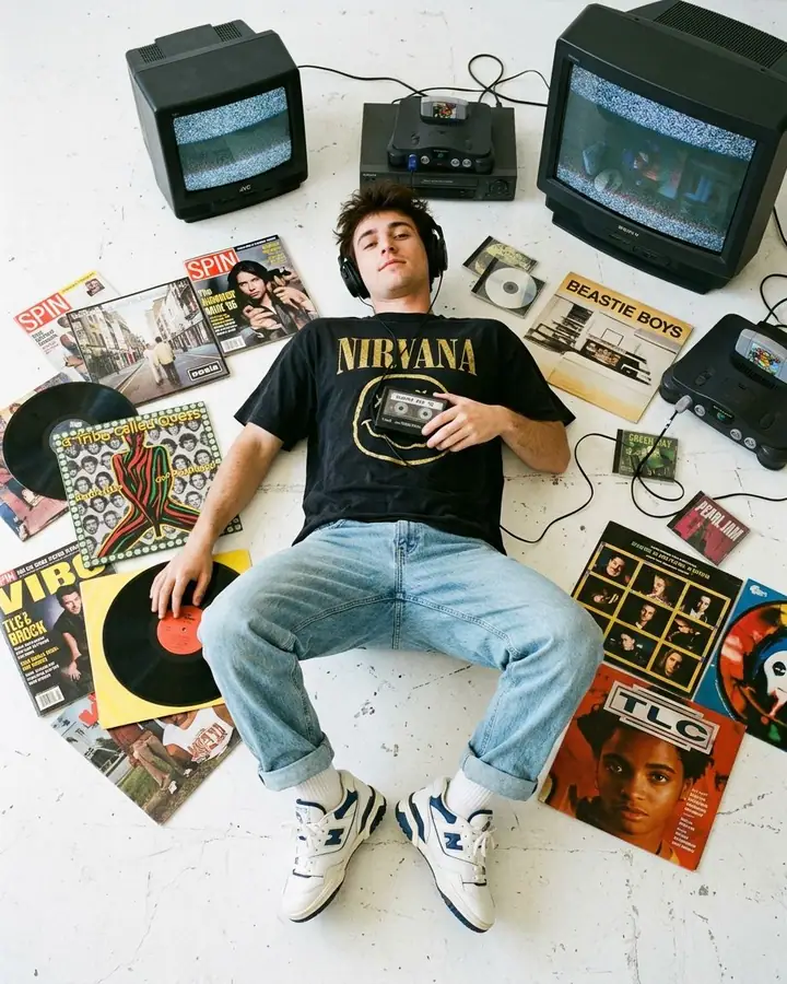Young man in 90s clothes lying on a white floor surrounded by vinyl records and CRT TVs