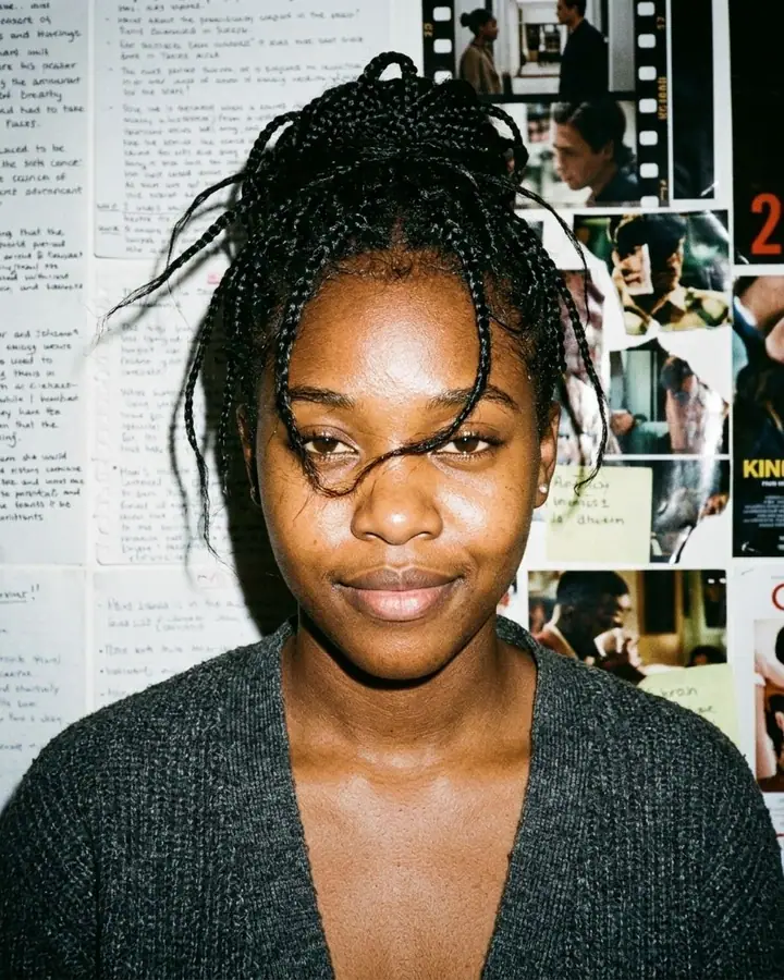Woman with pinned hair and a half-smirk lit by harsh flash in front of handwritten notes