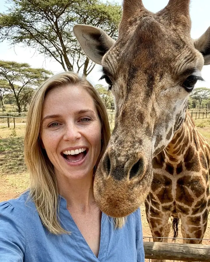 AI example of a woman laughing in a selfie as a giraffe leans into the frame